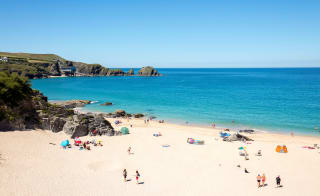 An aerial view of Padstow beach. Holiday goers are on the beach and in the sea. A bright blue sky is above the sea. image