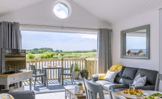 The lounge area of The Meadow Lakeside Lodge at The Bay Filey, which leads out to the decking area overlooking the lake on a sunny day. image