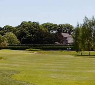 A photo of the green grassy grounds to a golf course on a cloudy day. There are fully grown trees either side of the photo. image