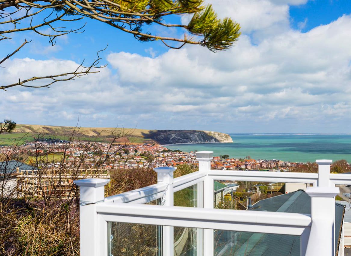 A view of the surrounding area from the balcony of one of our stunning holiday homes at Swanage Bay View. There is a view of the sea in the distance on a cloudy summers day. image