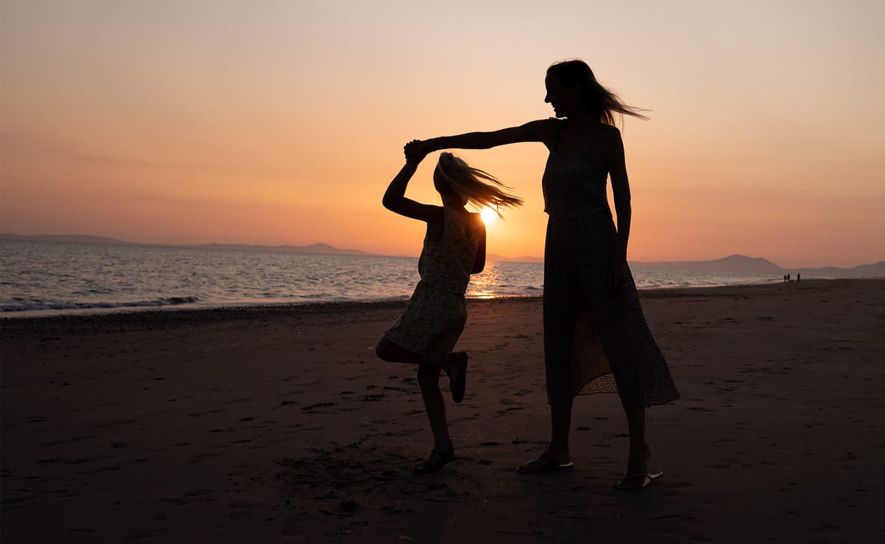 A mother and daughter dancing on the beach at sunset. image
