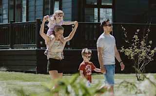 A young family taking a stroll past our stunning holiday homes with roof terraces. One of the two children is on their mum's shoulders. image