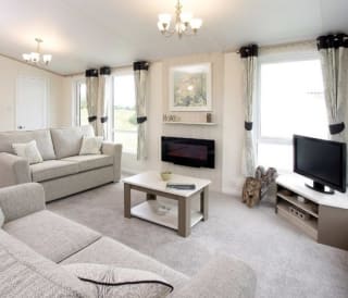 The interior of one of our Luxury holiday lodges. There are two large sofas, a TV, and plenty of space around a coffee table.