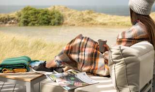 A lifestyle image of a woman relaxing on the decking at our stunning holiday park in Cornwall, St Ives Bay. There are views of the ocean in the background.