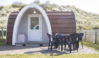 Exterior of our camping pod at St Ives Bay, Cornwall. A table and chair is located on the right, the perfect spot for brunch in the sunshine. image