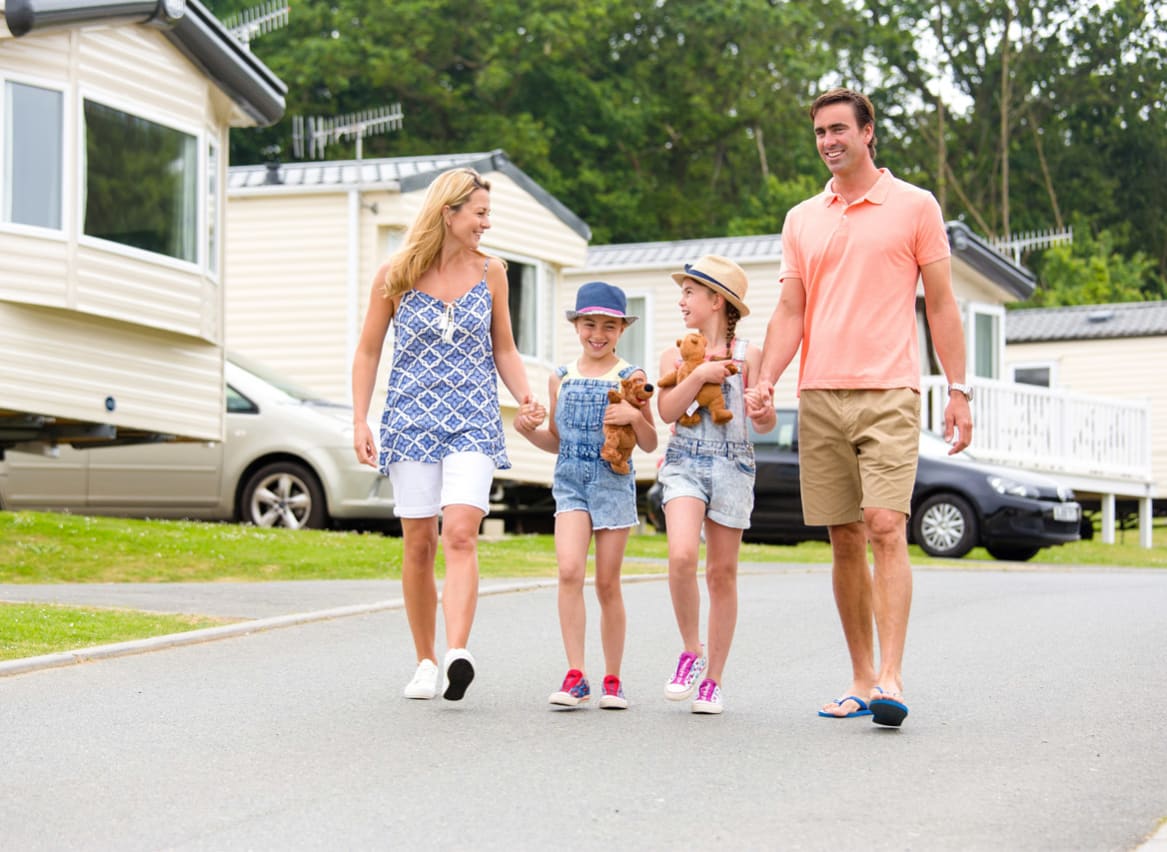 A family holding hands walking through one of our stunning holiday pars. There is a row of caravans in the background. image