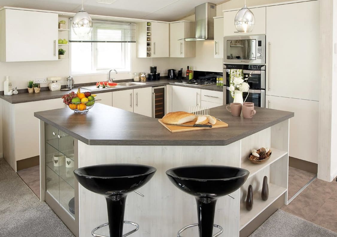 The interior of one of our Luxury holiday lodges. There's a kitchen area with many appliances, and an island in the centre.
