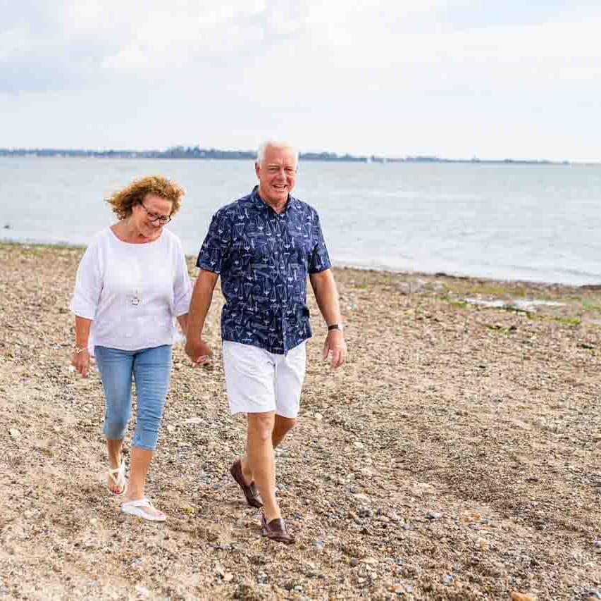 A mature hetero white couple are walking along the sands of Mersea Island beach, Essex.
