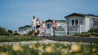 A young family playing outside on a sunny day. There is a row of caravans in the background.