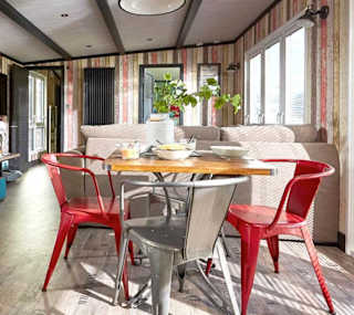 An image of the interior of one of our holiday lodges. There's wooden panneling, a cream fabric sofa and red metal dining chairs around a wooden table. image