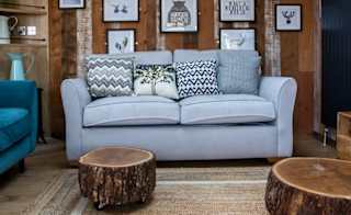 An image of the interior of one of our luxury holiday lodges as part of the May Bank holiday offer. The walls have wood panneling and there's pair of blue and grey two seater sofas. image