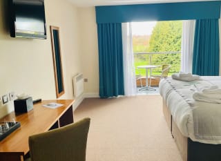 The interior of a room at Boston West Hotel. There is a large double bed, a TV, and a balcony with chairs and a table. image