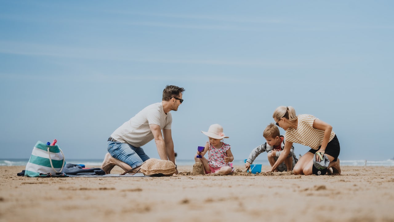 A young family enjoying a sunny day on the beach, playing in the sand.