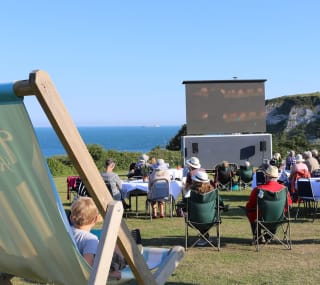 A group of people enjoying the outdoor cinema at our stunning holiday park on the Isle of Wight, Whitecliff Bay. There are views of the sea in the background on a summers day. image