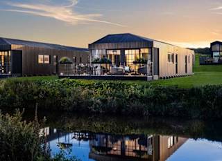 The outside of one of our Retallack holiday barns. The evening sun is shining on the holiday home, which is situated right near a peaceful lake. image