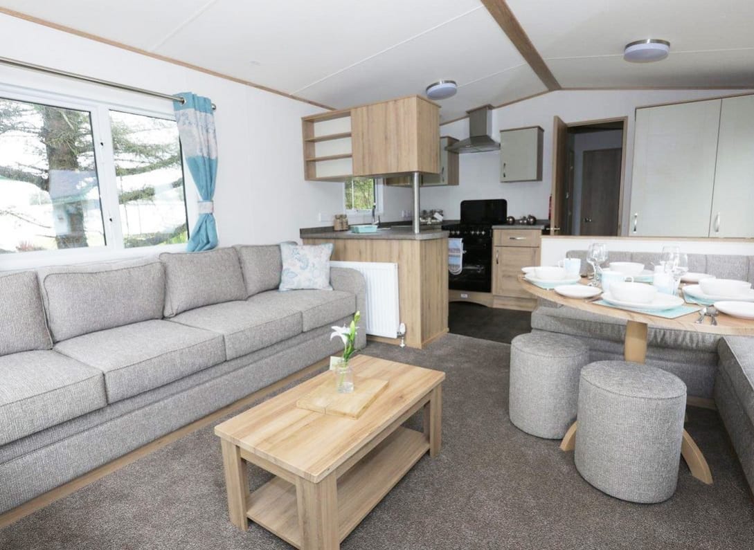 Suggested: The interior of one of our luxury caravans. There's a large, grey sofa, a seating area with a table, and a kitchen space with several appliances. image
