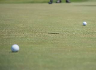 A close up image of two tennis balls at Playgolf Colchester. There are two people standing in the background. image
