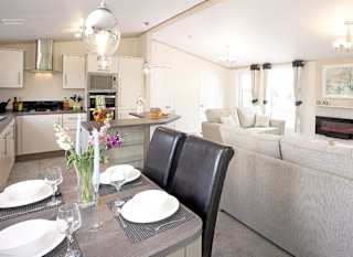 The interior of one of our Luxury holiday lodges. There's a dining area, kitchen section, and two grey sofas. image