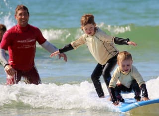 Two children surfing in the sea with an instructor from Shore Surf. image