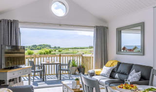 The lounge area of The Meadow Lakeside Lodge at The Bay Filey, which leads out to the decking area overlooking the lake on a sunny day. image
