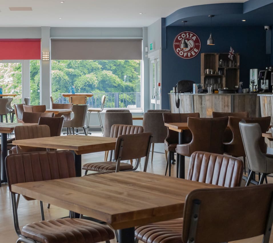 The seating area at The View Bar & Coffee Lounge at our Dorset holiday park, Swanage Bay View. There are tables and chairs and a view of the bar and Costco Coffee sign in the background. image