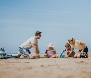 A young family enjoying a sunny day on the beach, playing in the sand.