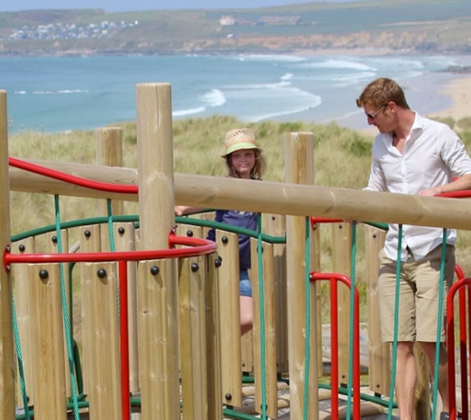 A father and son playing in the outdoor playground at our St Ives Bay Holiday Park with views of the sea in the background. image