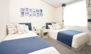 The interior of one of our Luxury holiday lodges. There's a twin bedroom with side tables and photos on the wall. image