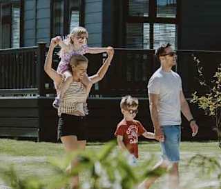 A young family taking a stroll past our stunning holiday homes with roof terraces. One of the two children is on their mum's shoulders.
