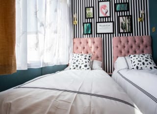 A single bed with cow spot print and light pink duvet covers and pillow. The wall behind it has black and white thin stripes. image