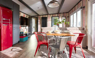 An image of the interior of one of our holiday lodges. There's wooden panneling, a cream fabric sofa and red metal dining chairs around a wooden table. image