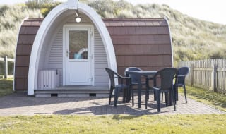 Exterior of our camping pod at St Ives Bay, Cornwall. A table and chair is located on the right, the perfect spot for brunch in the sunshine. image