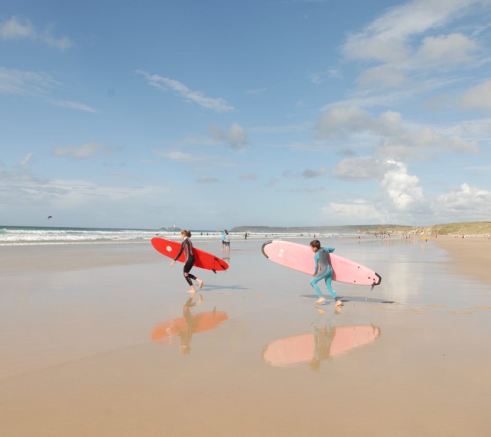 Two children running on the beach with surf boards towards the sea. image