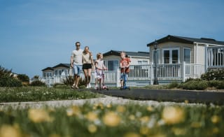 A young family playing outside on a sunny day. There is a row of caravans in the background. image