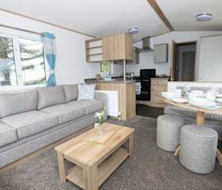 Suggested: The interior of one of our luxury caravans. There's a large, grey sofa, a seating area with a table, and a kitchen space with several appliances.