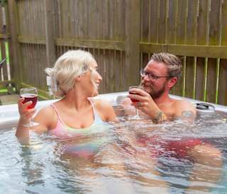 A couple soaking into the bubbles in their own private hot tub at one of our stunning holiday homes at Piperdam, Scotland. The dog is resting it's head on the hot tub.