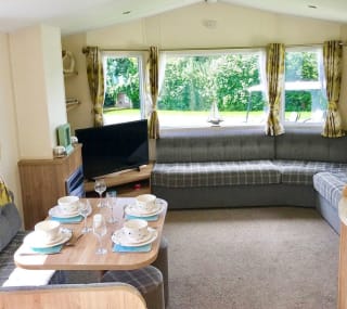 The interior of one of our Superior caravan holiday homes. There’s a large sofa, flatscreen TV, and a comfortable dining area. image