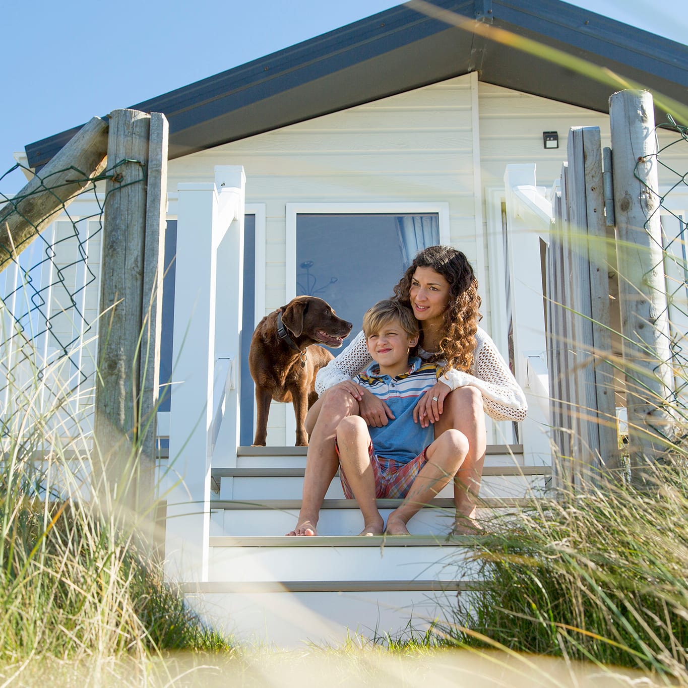 A mother, son and their chocolate lab dog sitting on the steps of one of our static caravans.