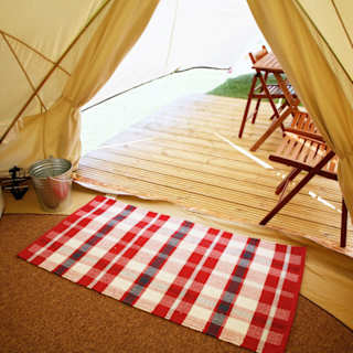 A photo of the living space inside of a canvas bell tent. To the left of the photo is a silver TV propped up on a white box. In the background is the entrance to the bell tent.