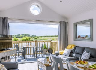 The lounge area of The Meadow Lakeside Lodge at The Bay Filey, which leads out to the decking area overlooking the lake on a sunny day. image