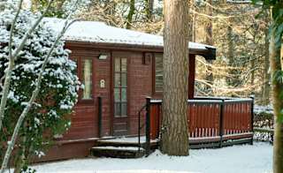 The exterior of one of our wooden lodges at Sandy Balls, Hampshire, on a snowy day. image