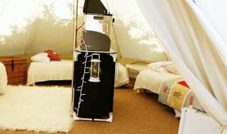A photo of the living space of a canvas bell tent. There is a brown woven floor mat and on top of this is a white faux fur rug. There is seating arranged in a semicircle. image