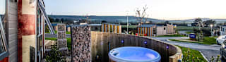 The outside of one of our holiday parks, which has an empty hot-tub behind a private fence. The sun is setting behind the wide view of the holiday park. image