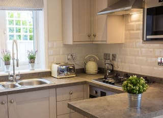 A kitchen area in one of our cottages. Off-white cabinets and grey stone worktops create a clean, welcoming space. Ontop of the worktop is a cream kettle and matching toaster. image