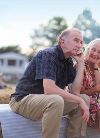 An older couple sat on a hay bale on a sunny day.