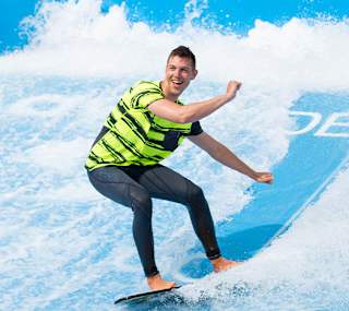 A young male is surfing on a wave stimulator with two other males watching from the sideline. image