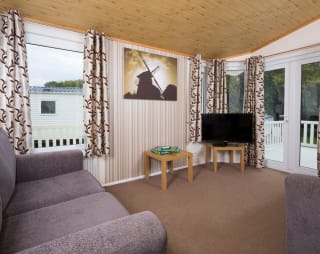 The interior of one of our Superior lodges. There are two grey sofas, a TV, and double-doors leading outside.