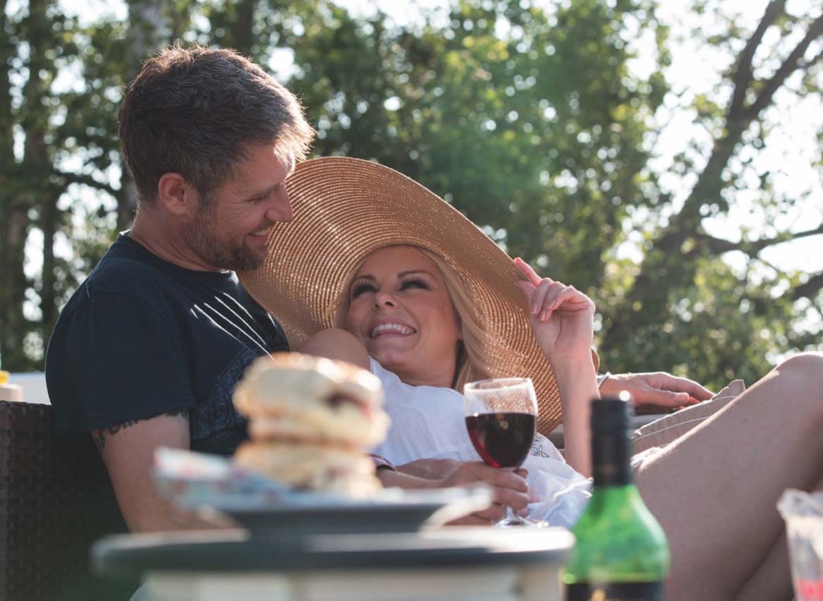 A couple sat outside in the sunshine enjoying a drink of red wine and some tasty treats. image