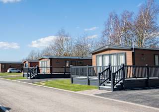 A photo of a row of wooden holiday lodges at our holiday park Appletree, Lincolnshire on a cloudy sunny day.