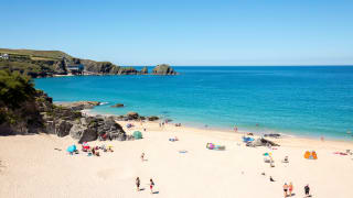 An aerial view of Padstow beach. Holiday goers are on the beach and in the sea. A bright blue sky is above the sea.
